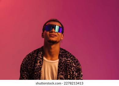 Young smiling african man wearing sunglasses   leopard shirt posing isolated over pink neon background