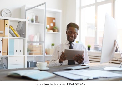 Young Smiling African-american Broker With Tablet Looking Through Online Rates On Brokerage Websites