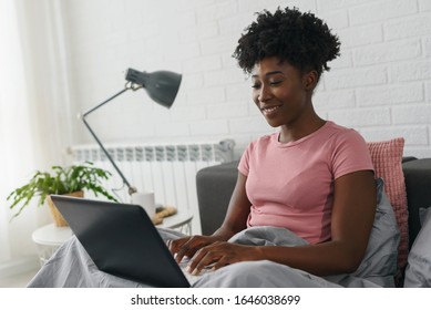 Young smiling African-American woman using laptop computer in the bed in the morning. Everyday use of technology concept. - Shutterstock ID 1646038699