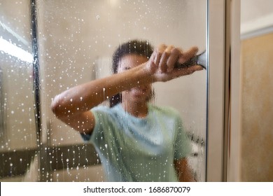 Young Smiling Afro American Woman In Uniform Cleaning Shower Door With Squeegee And Spray Detergent. Cleaning Service Concept. Housework