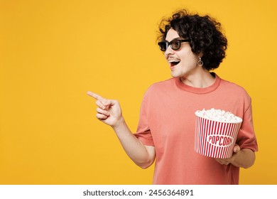 Young smiling amazed happy man he wear pink t-shirt casual clothes 3d glasses watch movie film hold bucket of popcorn in cinema point finger aside isolated on plain yellow background studio portrait - Powered by Shutterstock