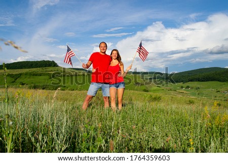 Young smiling American couple family man, woman, girlfriend holding each other celebrating in nature after coronavirus pandemic in freedom Independence Day 4 4th fourth of July with two US USA flags