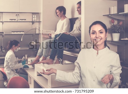Young smiling american  nail salon master inviting clients to procedure