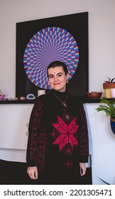 Young And Smiling Artist Girl With Very Short Hair, Bindi And Wool Sweater In Front Of His Beautiful Abstract Circle Painting