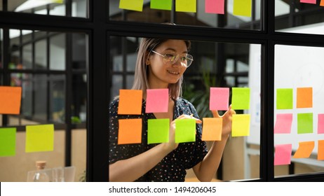 Young smiling asian business woman mentor leader write tasks creative ideas on sticky post it notes on glass wall, vietnamese female coach planning project corporate management on sticker scrum board - Shutterstock ID 1494206045