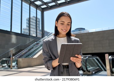 Young smiling Asian business woman entrepreneur wearing suit holding digital tablet standing in city metro using wireless internet technology on pad computer, working online in subway. - Shutterstock ID 2179380691