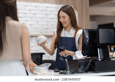 Young smiling Asian female cashier at the supermarket cashier using barcode scanner - Powered by Shutterstock