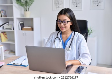 Young Smiling Asian Female Doctor Looking At Laptop Screen Holding Online Consultation With Patient Or Training Webinar. Telemedicine Remote Medical Appointment, E-learning Concept