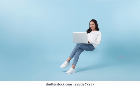 Young smiling Asian girl student floating in mid-air with using laptop isolated on blue studio copy space background. - Shutterstock ID 2280269237