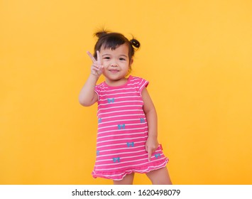 Young Smiling Asian Girl Wearing Striped Dress Holding Hands Up With Two Fingers Looking At Camera.