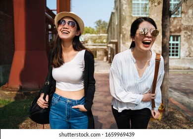 young smiling asian japanese women in sunglasses walking and talking in sunset time outdoor. Happy best friends laughing and having fun while relax in old city street. tourists sightseeing in summer