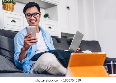 Jovem sorridente homem asiático relaxante usando computador portátil trabalhando e videoconferência reunião em casa.Jovem homem criativo olhando para a mensagem de digitação de tela com smartphone.work from home concept