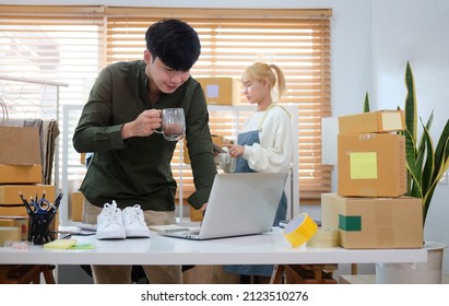 Young Smiling Asian Man Small Business Owner Working On Laptop Computer At Warehouse.