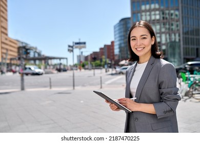 Young Smiling Asian Professional Woman Wearing Suit Holding Digital Tablet Corporate Digital Information Global Technology Standing On Big City Street Using Pad Computer Outside. Portrait