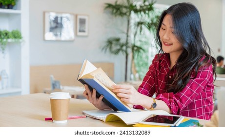 Young smiling asian woman looking reading an book, dressed in a red white striped shirt with long brown hair, soft photo of beautiful. tablet computer and a pen at a study desk. out of focus. - Powered by Shutterstock