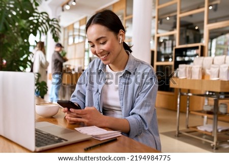 Young smiling Asian woman student using smartphone for elearning wearing earbud, watching online class webinar training in mobile app, studying, having hybrid remote video call on cell phone.