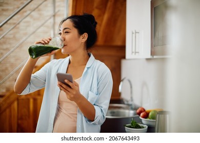 Young smiling Asian woman using smart phone while drinking detox smoothie in the morning at home. - Shutterstock ID 2067643493