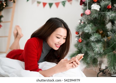 Young Smiling Asian Woman Is Using Mobile Phone. Christmas And New Year Time