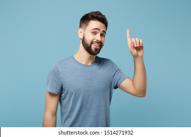 Young smiling attractive man in casual clothes posing isolated on blue wall background, studio portrait. People sincere emotions lifestyle concept. Mock up copy space. Pointing index finger up - Shutterstock ID 1514271932