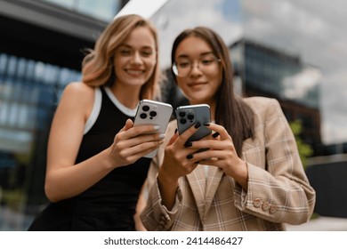 young smiling attractive women standing outside in street doing business, education, students working together, asian and blond, casual style, using smartphone - Powered by Shutterstock