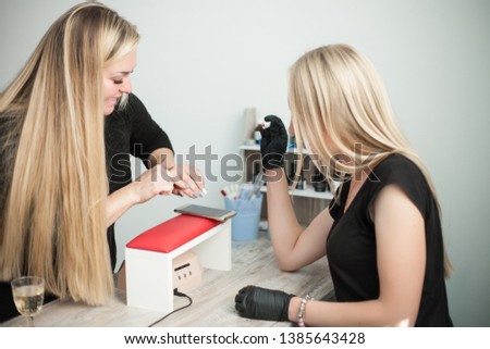 Young smiling beautician woman manicurist talking to a female client, does manicure, woman choosing a color of nail polish.