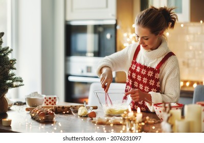 Young smiling beautiful woman in apron making dough for christmas gingerbread cookies while cooking in cozy decorated kitchen, happy female cooking during winter holidays, making xmas sweets - Powered by Shutterstock