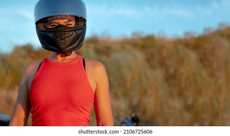 Young Smiling Biker Woman Wearing Red Tank Top And Black Motorcycle Safety Helmet. Copy Space