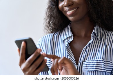 Young smiling black African woman holding smartphone in hand looking at cell phone device using mobile application technology for texting, banking, money transfer or shopping online. Close up view - Powered by Shutterstock
