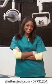 Young Smiling Black Ethnic Afro-American Female Dentist Assistant Standing In Dental Office By Chair