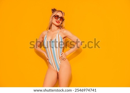 Young smiling blond model in summer swimwear colourful bathing suit. Sexy carefree woman having fun and going crazy. Female posing near yellow wall in studio. Cheerful and happy