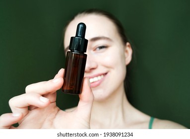 A Young Smiling Blonde Shows A Bottle Of Face Serum Into The Camera.Tea Tree Oil . Selective Focus.