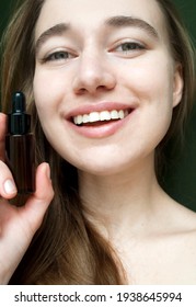 A Young Smiling Blonde Shows A Bottle Of Face Serum With Tea Tree Oil At The Camera. 