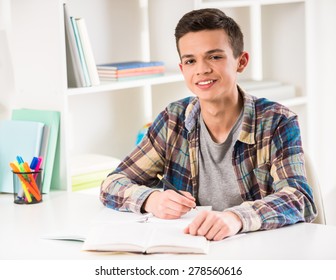 Young smiling boy sitting at the table and doing homework at home.