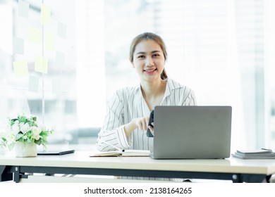 Young smiling business Asian young woman using smartphone near computer in the office, copy space