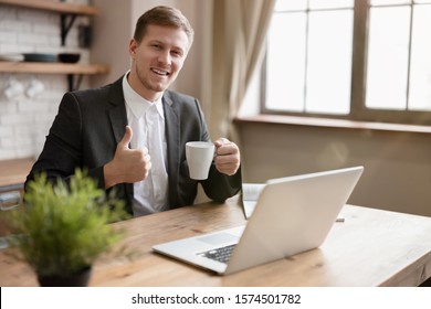 young smiling business man checking mail in laptop in the kitchen while drinking hot tea before going to work shows like sign . multitasking, morning.