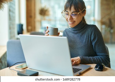 Young Smiling Business Woman In Spectacles Working On Portable Laptop Computer. Female Copywriter Sitting At Desk And Typing On Keyboard, Working On Project, Writing Down Ideas Into Netbook