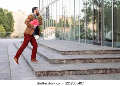 Young Smiling Businessman Carrying Documents And Calling While Moving Forward. Man In Casual Clothes Walking Near Modern Office Building, Full Length, Copy Space. Business And Success Concept