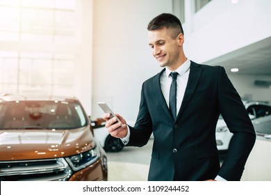 Young Smiling Businessman In Formal Wear With Phone In Hand While Buying A New Car In Dealership