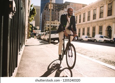 Young Smiling Businessman Going To Work By Bike. Man In Suit Riding Bicycle On Sidewalk In Morning.