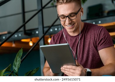 Young smiling businessman man guy manager freelancer male student using digital tablet and headphones watch new vlog or music videos webinar enjoy videocall talk choose audio book in modern coworking - Powered by Shutterstock