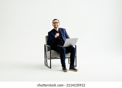 Young smiling businessman sitting in office chair and working on laptop computer isolated on white background - Shutterstock ID 2114135912