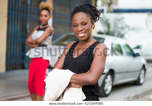 Young smiling businesswoman standing behind a\
car, arms crossed looking at\
camera