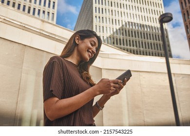 Young and smiling businesswoman standing on street when text messaging