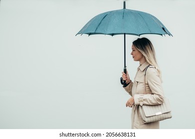 Young Smiling Businesswoman With Umbrella And Shoulder Bag Walking Down City Street During Rain