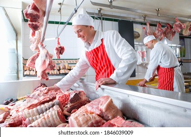 A Young Smiling Butcher Checking Meat In A Display Case In A Meat Shop.