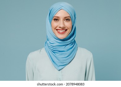 Young smiling calm confident arabian asian muslim woman in abaya hijab clothes look camera isolated on plain blue color background studio portrait. People uae middle eastern islam religious concept