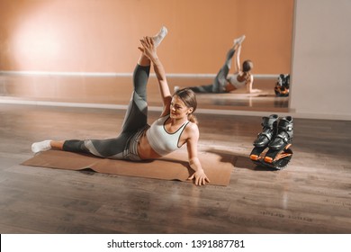 Young smiling Caucasian brunette stretching leg on mat in gym. Next to her jumps footwear. Do something today that your future self will thank you for.