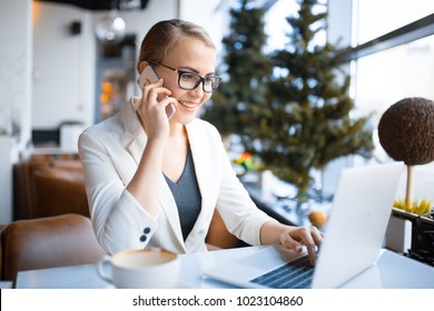 young smiling caucasian business woman talking on the phone while working at the laptop in the cafe