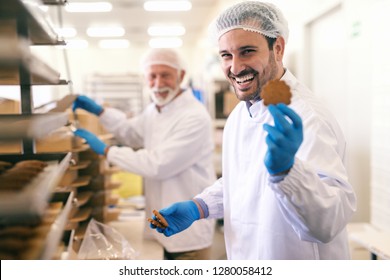 Young Smiling Caucasian Worker Showing Cookie While Standing In Food Factory.