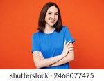 Young smiling cheerful fun cool happy woman she wears blue t-shirt casual clothes hold hands crossed folded looking camera isolated on plain red orange background studio portrait. Lifestyle concept